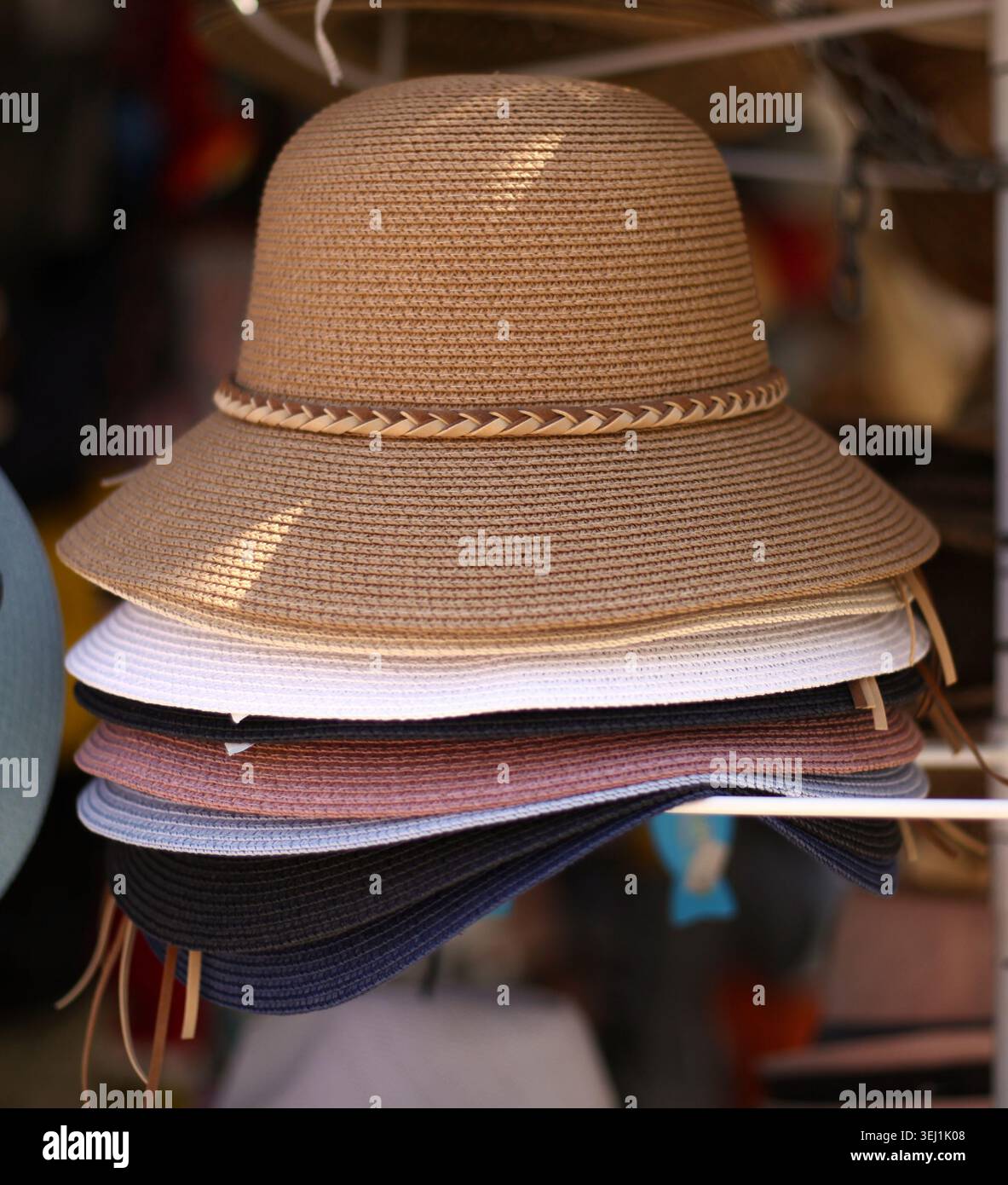 Primo piano di un assortimento di cappelli da sole in paglia da donna multicolore con fascia in pelle intrecciata marrone sul cappello di un mercato. Foto Stock