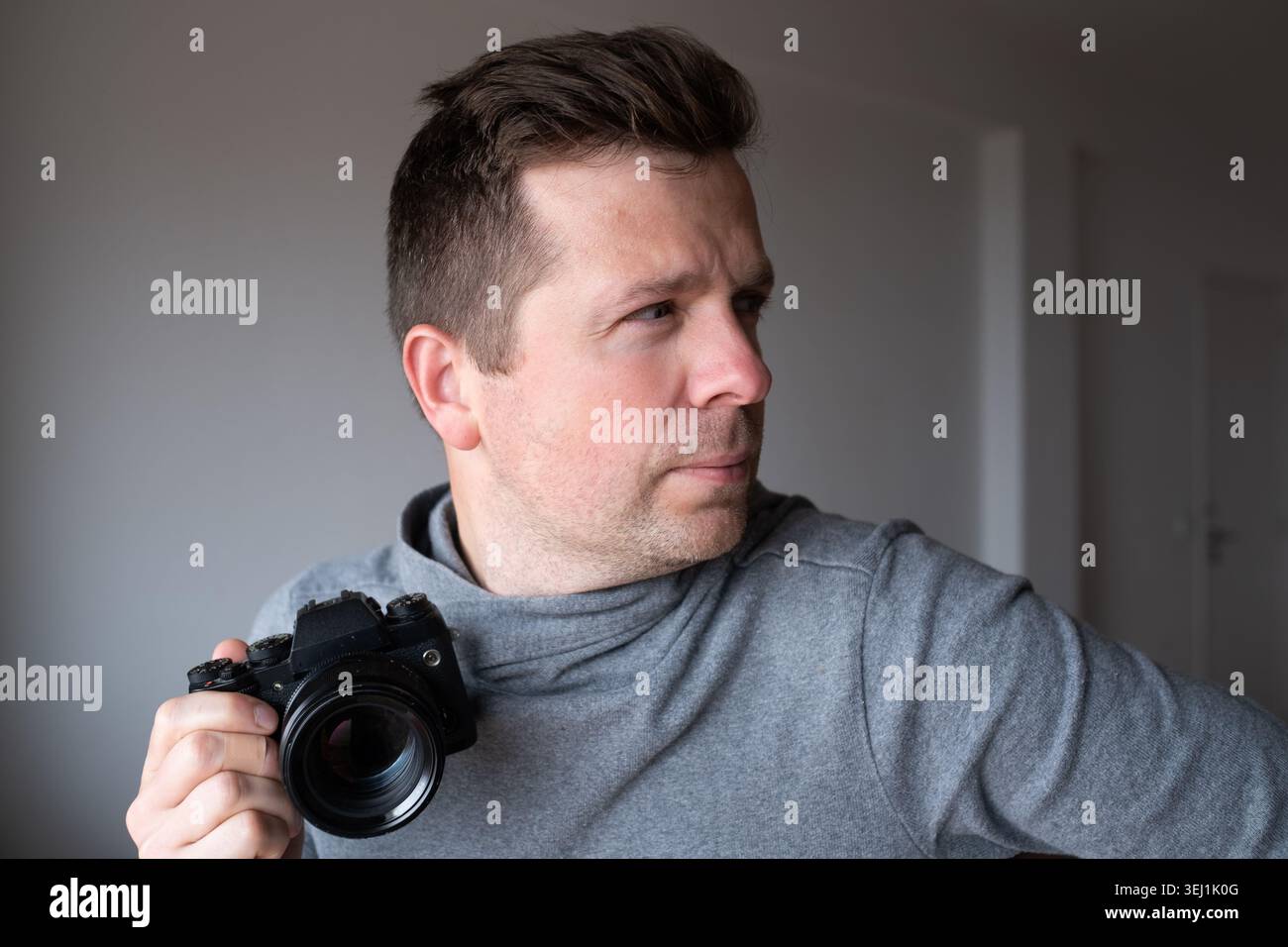Ritratto di un uomo concentrato con una fotocamera mirrorless digitale che guarda lateralmente. Foto Stock