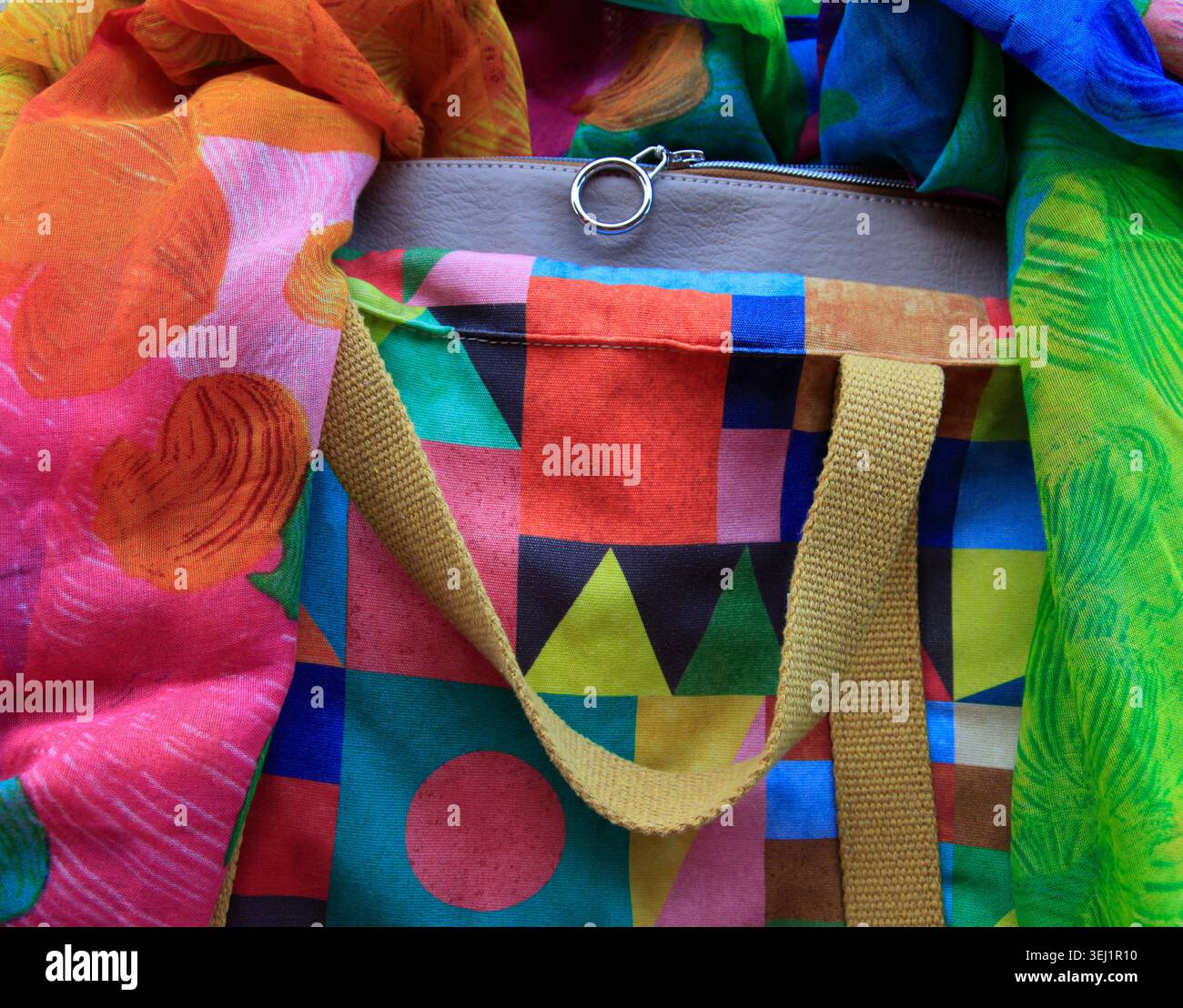 Borsa tote colorata e vivace con motivo patchwork geometrico, fiancheggiata da luccicanti sciarpe di seta Foto Stock