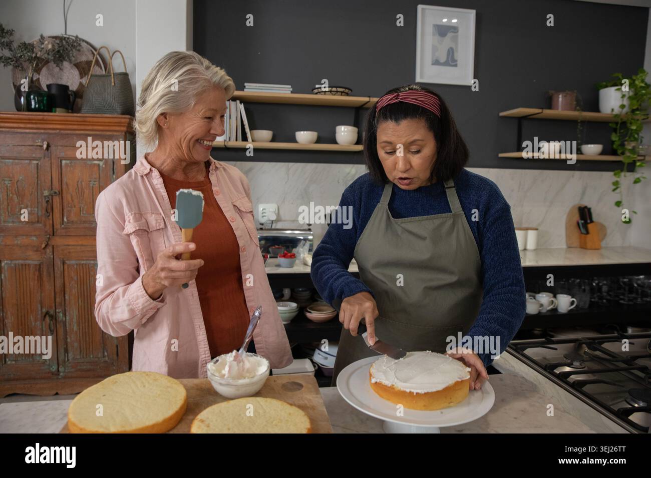 Due fornai maturi che indossano camicie color navy e rosa che glassa la torta sul bancone della cucina, tenendo in mano la spatola Foto Stock