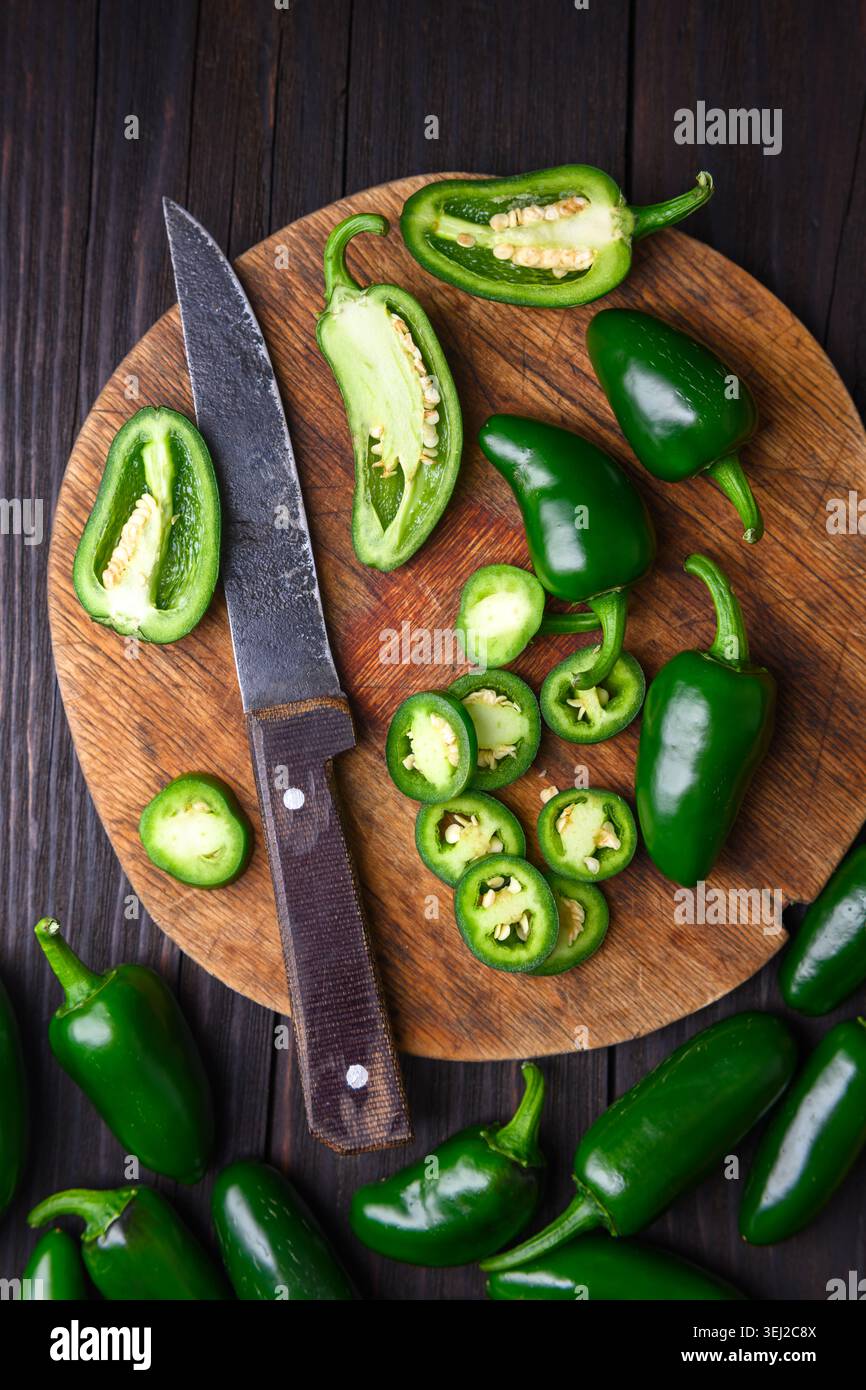 Peperoni di Jalapeno disposti con fette e coltello su tavola di legno. Preparazione di peperoncino verde fresco stile rustico Foto Stock