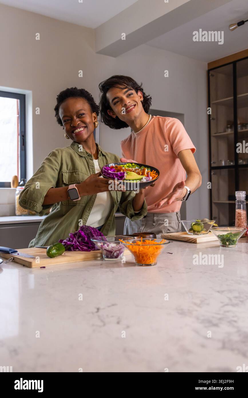 Amici diversi che presentano un piatto colorato per insalate al bancone della cucina con avocado, coltello e lime Foto Stock