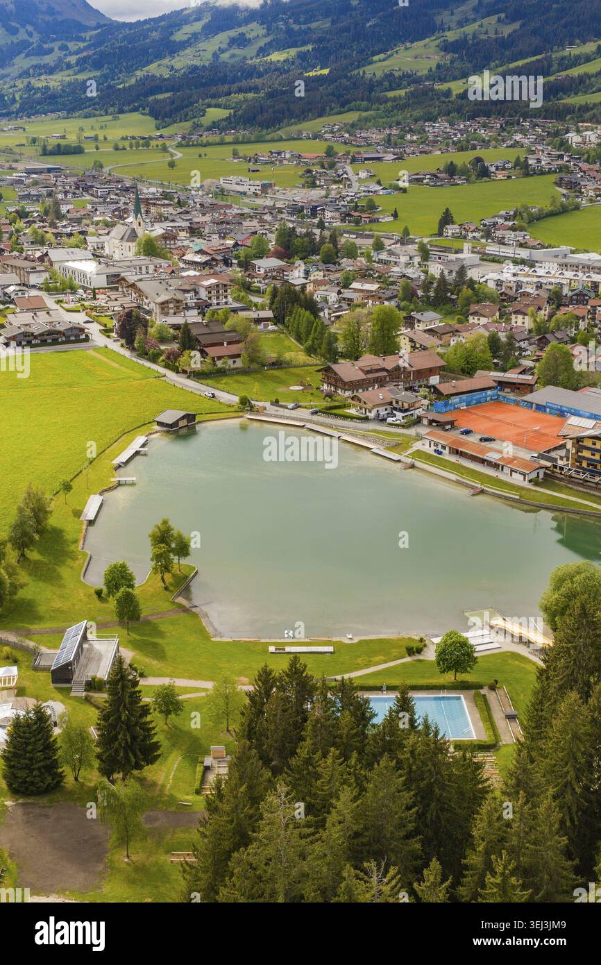 Villaggio alpino sul lago con prati verdi e colline, montagne sullo sfondo, vista aerea, Kirchberg, Austria Foto Stock