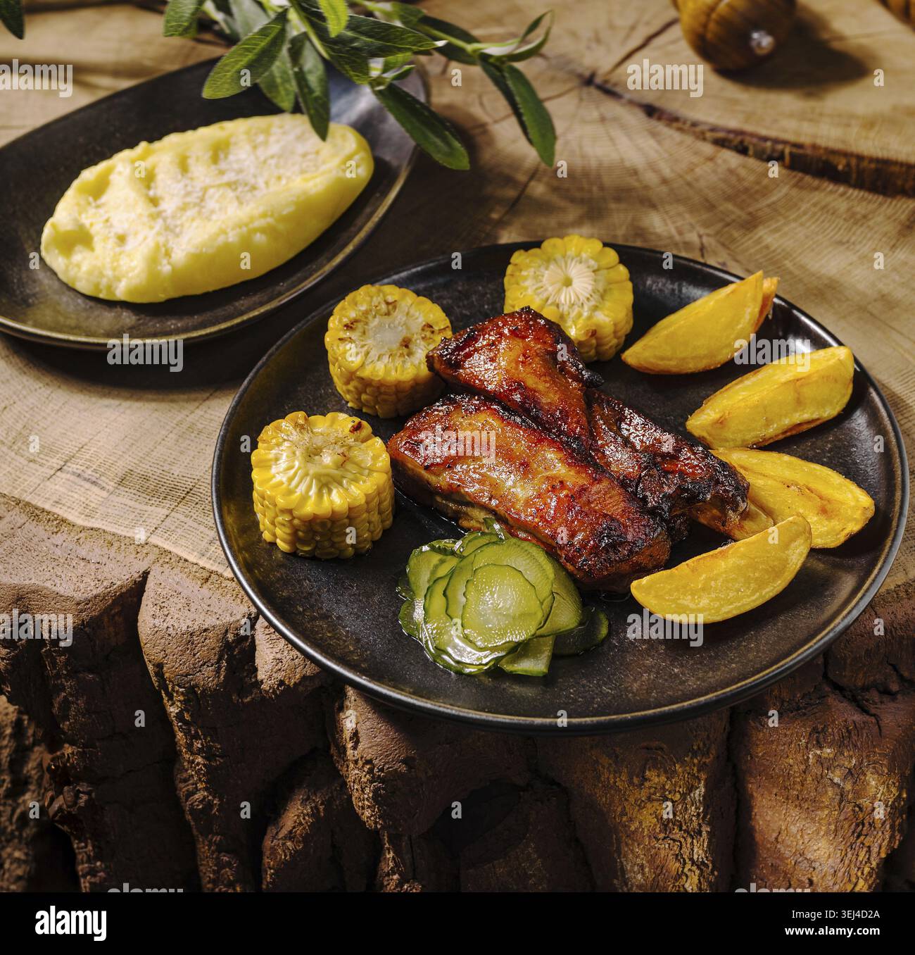 Cibo, costolette di maiale alla griglia servite con spicchi di patate arrosto, mais sulla pancetta e cetrioli sottaceto, con un lato di crema di patate sulla rus' Foto Stock
