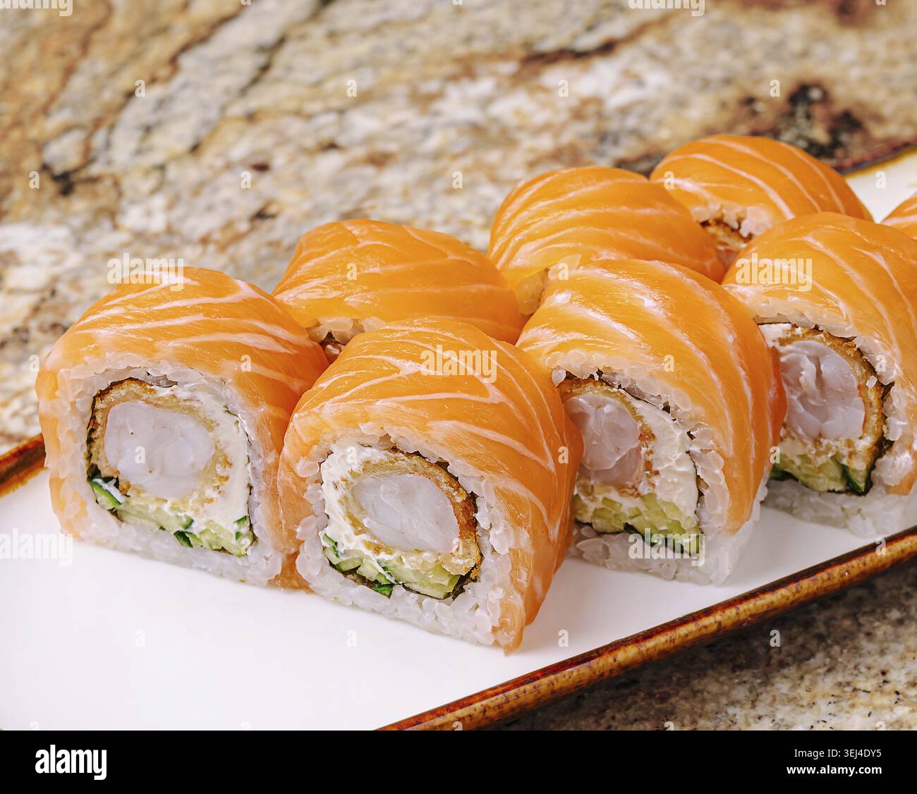 Cibo, deliziosi panini di sushi al nigiri con salmone fresco e ripieno croccante di granchio, serviti su un piatto bianco. L'ambiente è un ristorante dai toni caldi, perfec Foto Stock