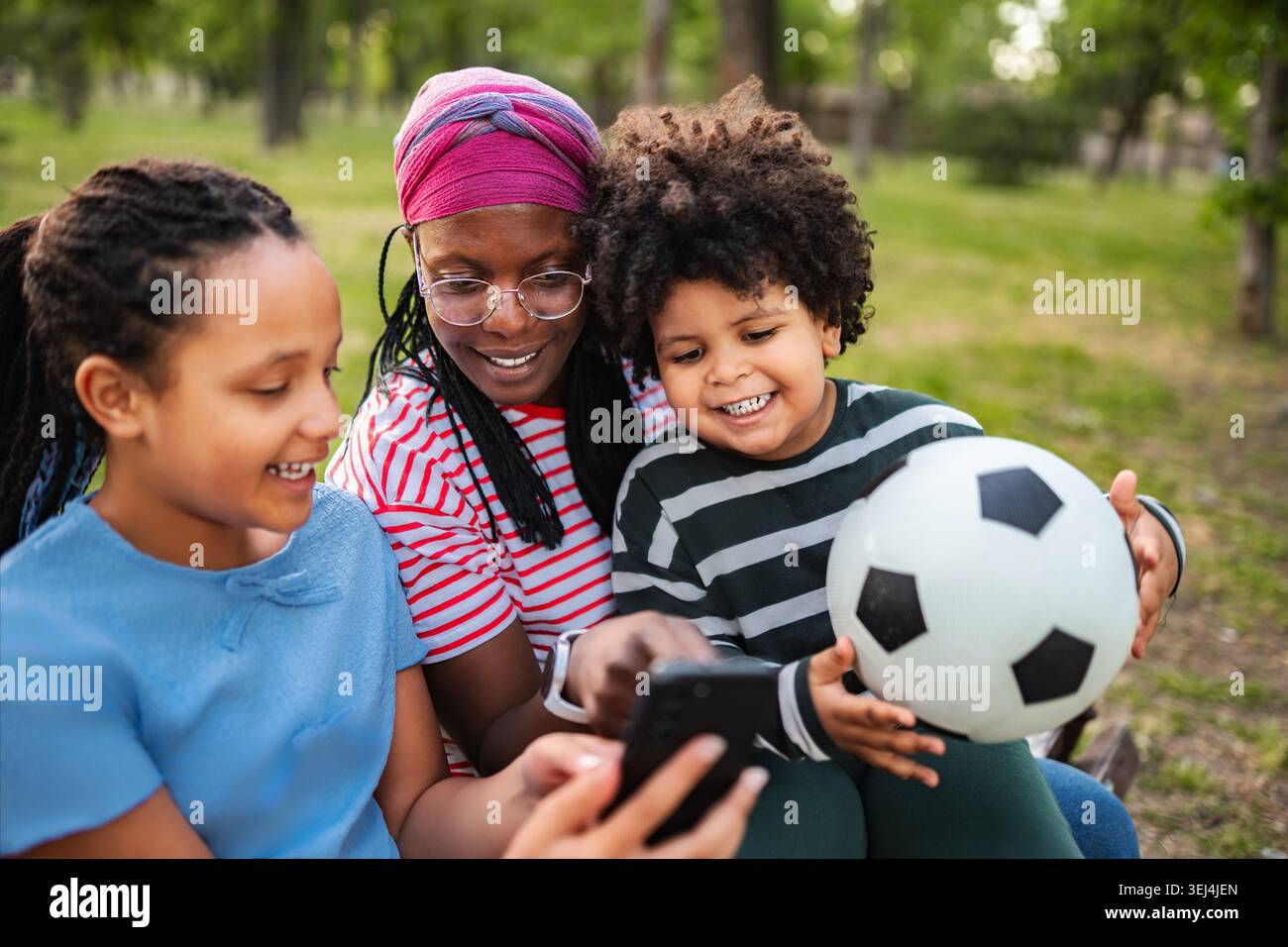 Madre e bambini guardano lo smartphone mentre si rilassano nel parco Foto Stock