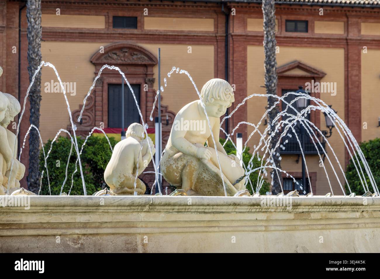 Siviglia, Siviglia - Spagna? 04-19-2024: Fontana in pietra AA con sculture per bambini, spruzzi d'acqua a forma di arco, illuminata dalla luce del sole Foto Stock