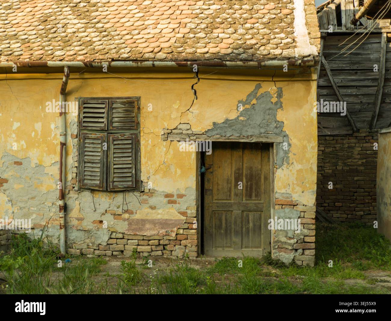 Facciata della vecchia casa con pareti gialle incrinate, porte in legno e persiane. Foto Stock