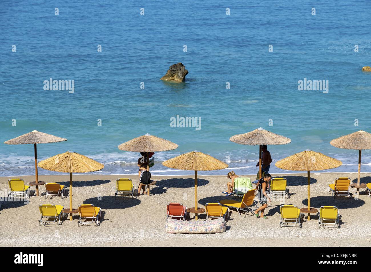 Nydri - Isole Ionie - Grecia - 08-09-2025: Spiaggia con ombrelloni di paglia, lettini gialli e arancioni, persone che si rilassano sulla spiaggia sabbiosa e tur Foto Stock