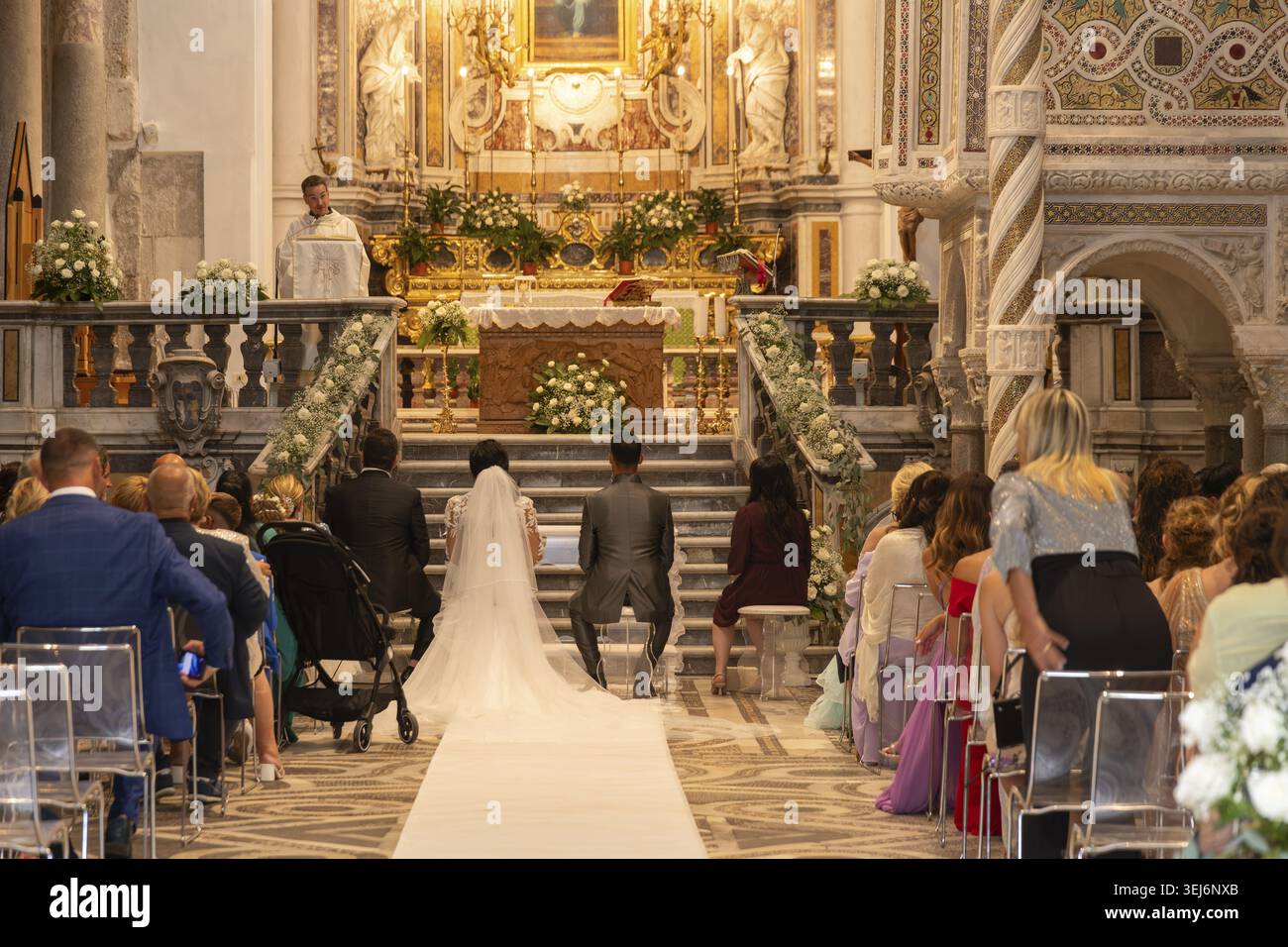 Sessa Aurunca - Campania - Italia - 08-29-2025: All'interno della Cattedrale di Sessa un sacerdote conduce una cerimonia nuziale mentre la coppia si inginocchia davanti all'alta ornata Foto Stock