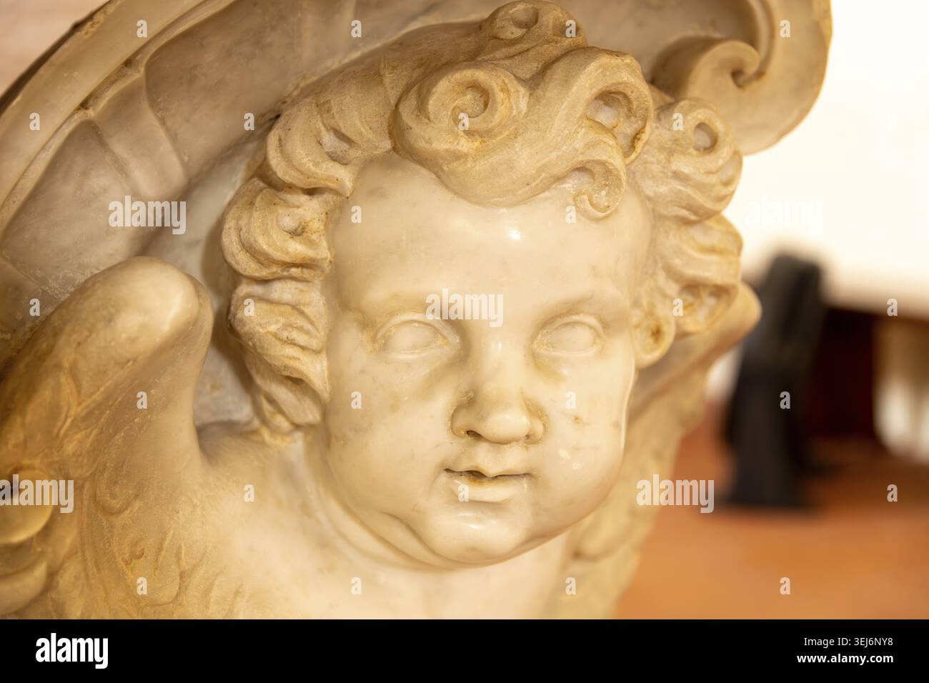 Sessa Aurunca - Campania - Italia - 08-29-2025: Primo piano di una testa di cherubino in marmo intagliato con morbidi ricci e piccole ali, che mostrano una liscia pietra invecchiata de Foto Stock
