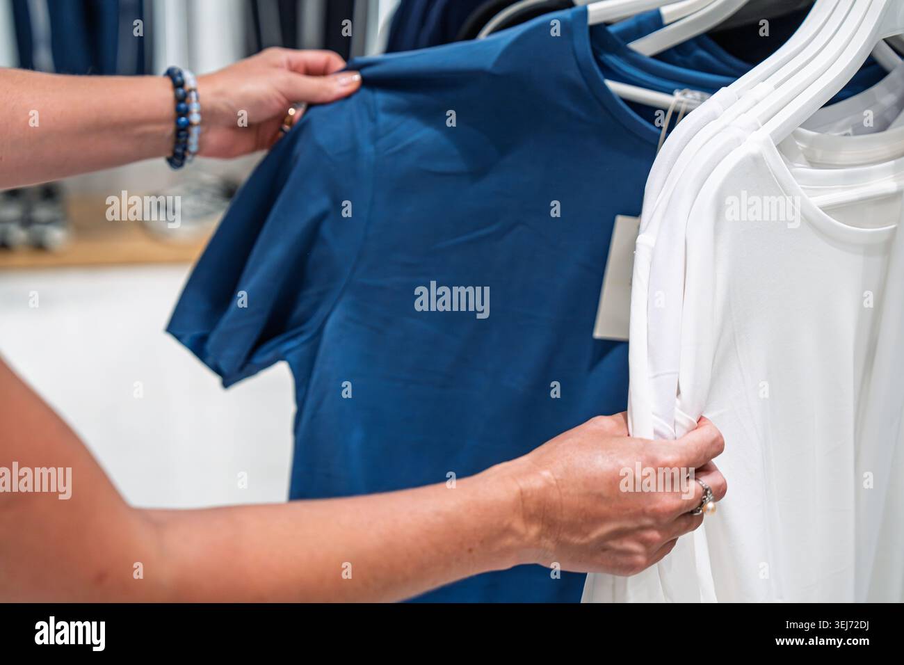 Donna che sceglie tra una t-shirt di base blu e una bianca mentre fa shopping e tiene in mano la maglietta blu Foto Stock