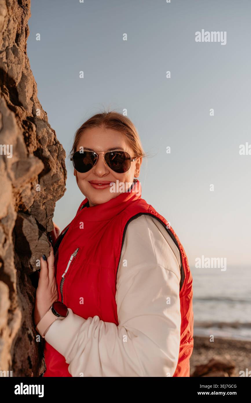 Occhiali da sole donna Coast sorridenti vicino a una scogliera rocciosa sulla spiaggia durante il tramonto con spazio fotocopie sopra il mare Foto Stock