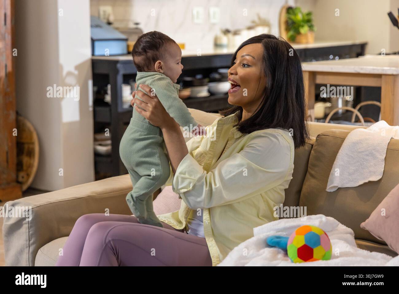 Madre e bambina afroamericana che sorride sul divano beige con onesie verdi Foto Stock