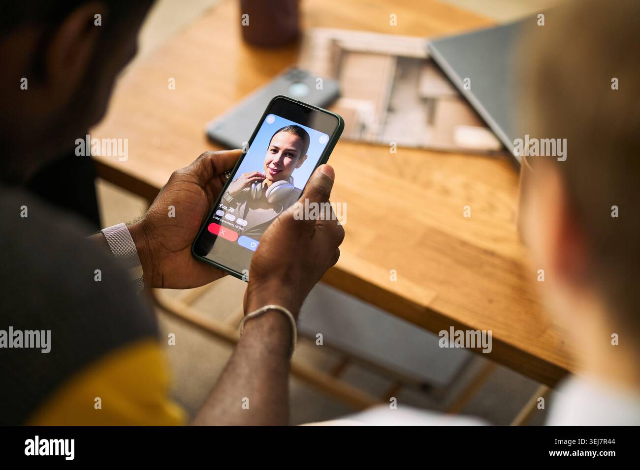 Vista a spalla di un giovane uomo adulto che tiene in mano lo smartphone, sfogliare il profilo di un'app di incontri accanto a un amico maschio, suggerire incontri online, connessione social, uso di app marketing Foto Stock