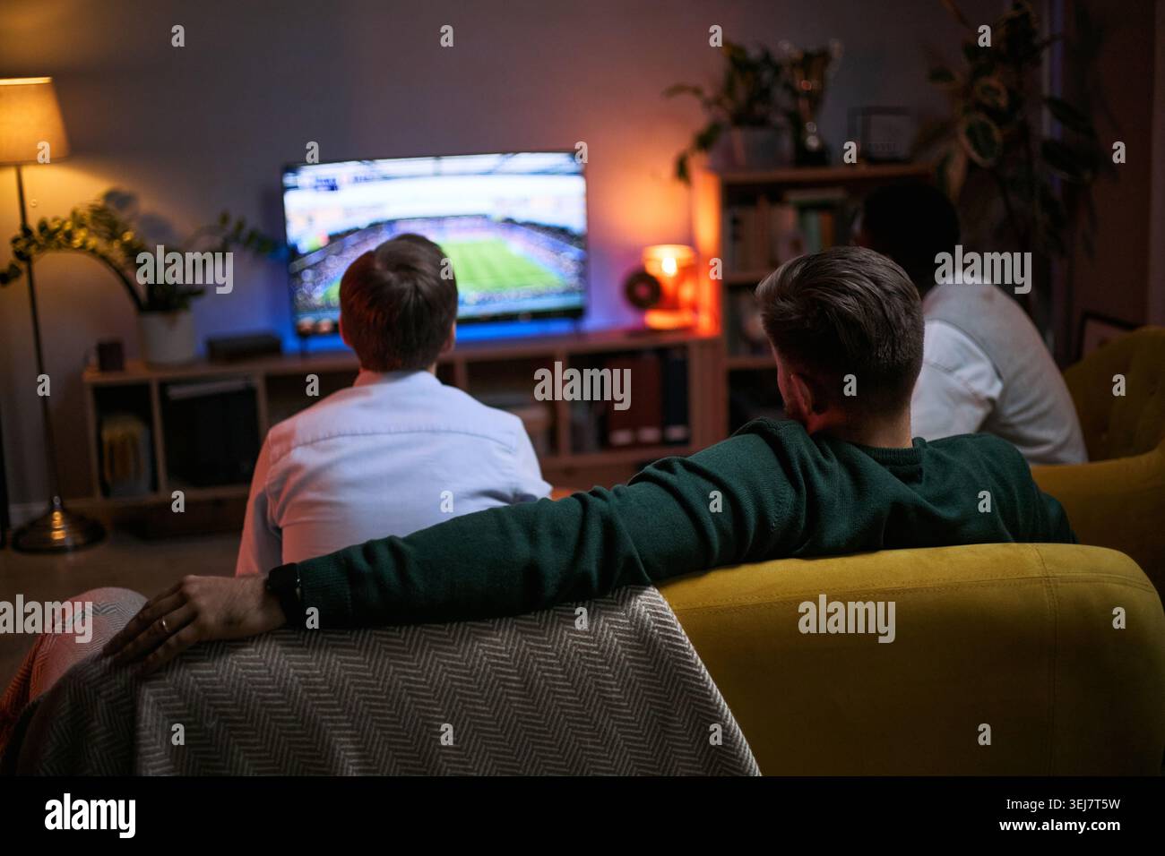 Giovani adulti che guardano la partita di calcio insieme a casa, esprimendo amicizia maschile, legame, tempo libero, lavoro di squadra. Ideale per il marketing sportivo, la connessione sociale e le campagne lifestyle Foto Stock