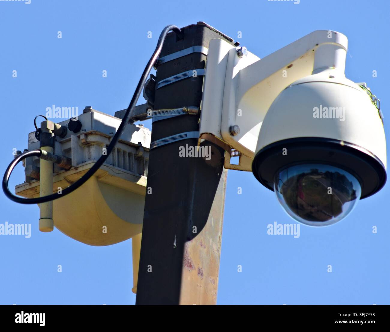 Primo piano di una telecamera di sicurezza montata su palo e di un'apparecchiatura di sorveglianza contro un cielo azzurro Foto Stock