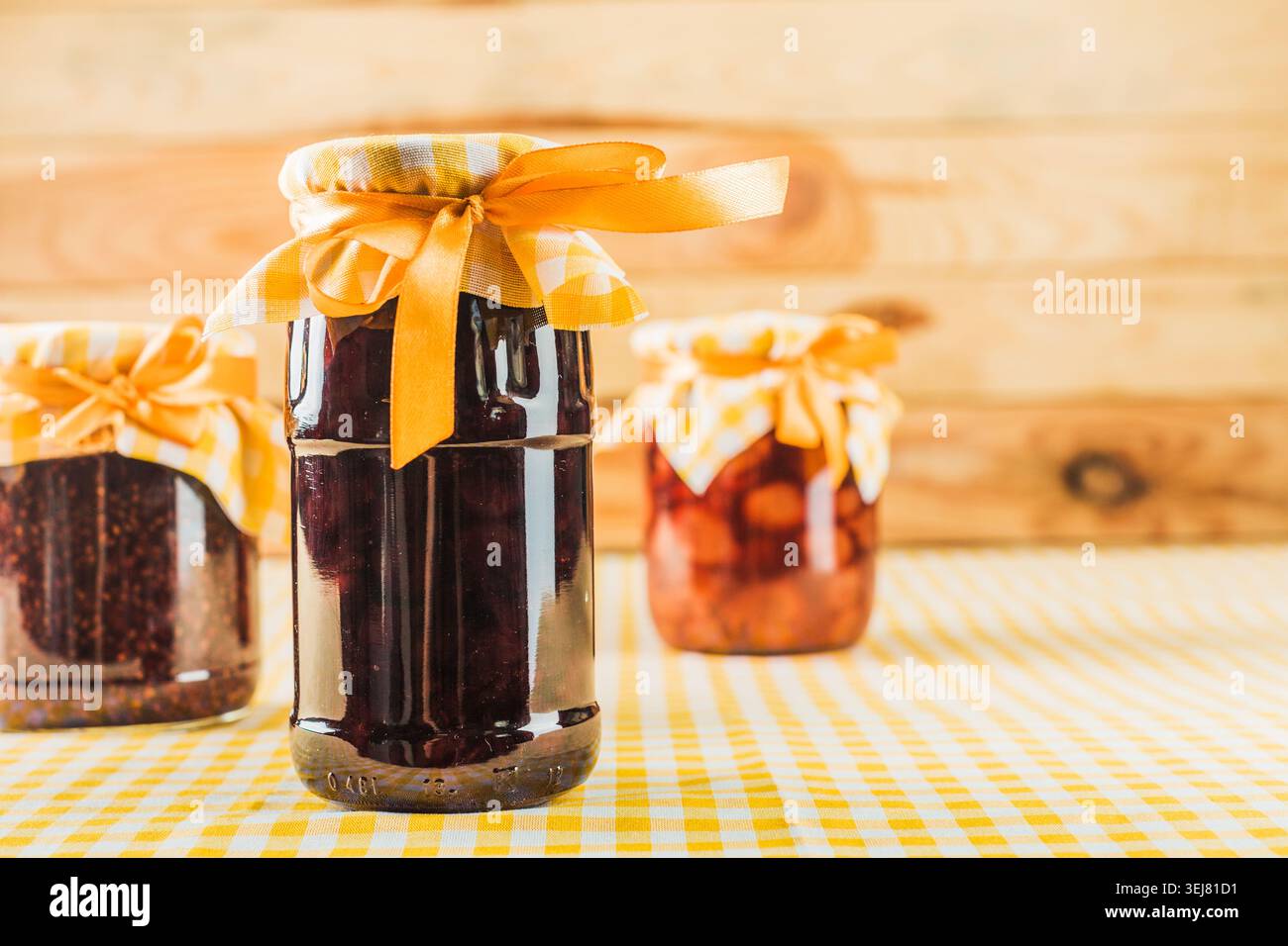 Vasetti di marmellata fatti in casa su una tovaglia a scacchi in cucina durante il giorno Foto Stock