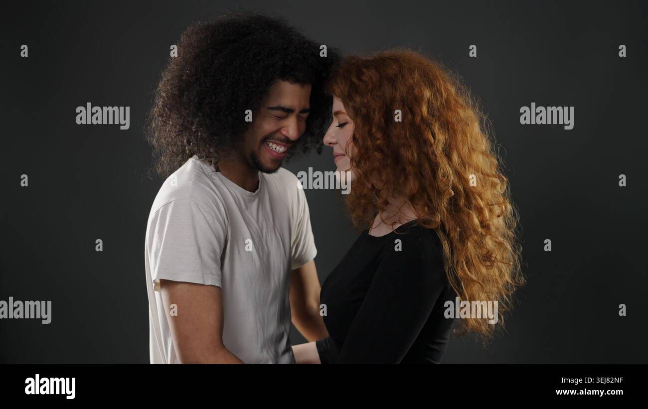 Coppia variegata con capelli ricci che sorridono e toccano la fronte, mostrando amore e connessione Foto Stock