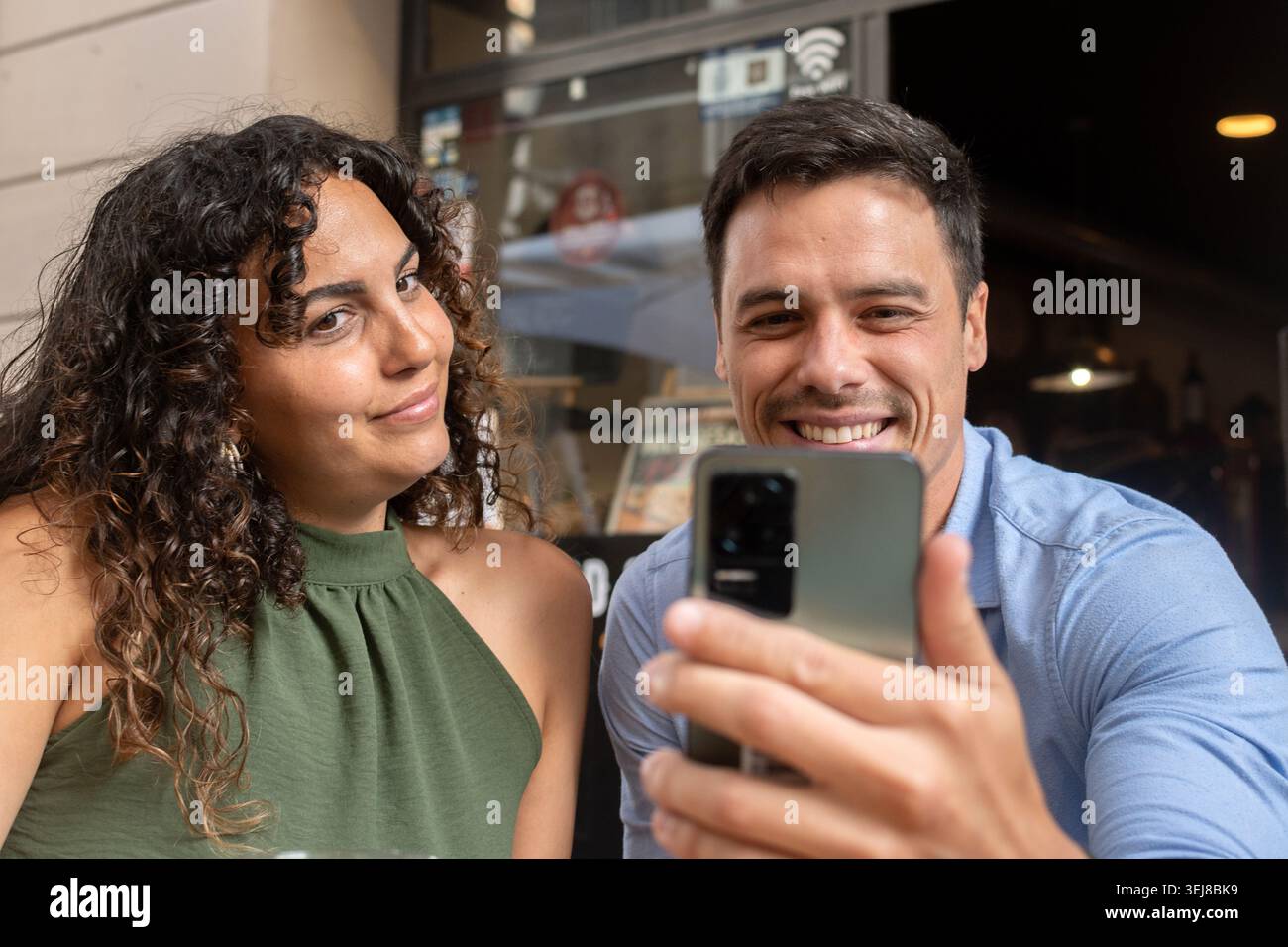 Una giovane coppia felice che si diverte insieme e si fa un selfie con uno smartphone nella terrazza di un ristorante all'aperto. Un momento di stile di vita informale con birra, Foto Stock