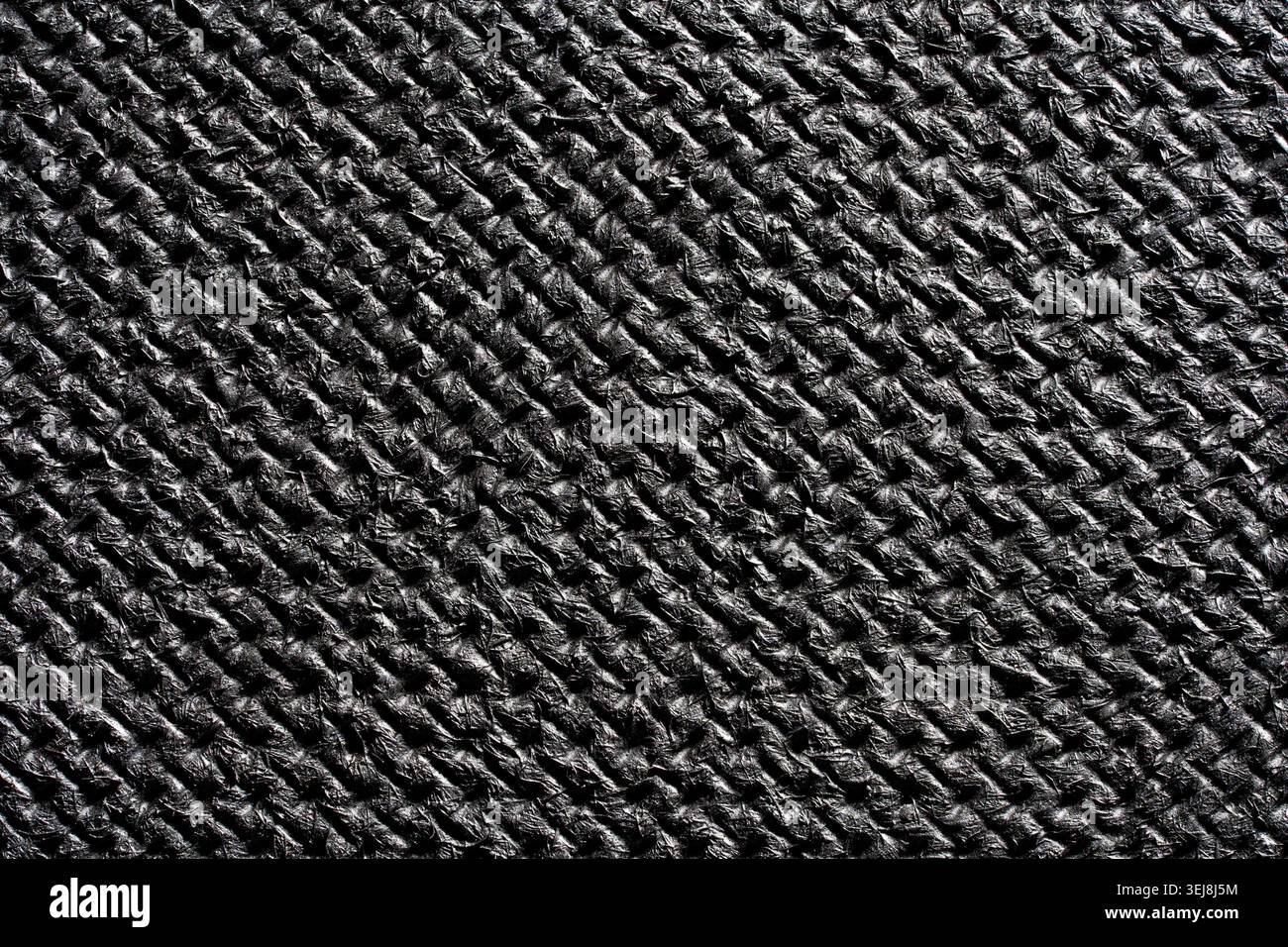 Primo piano della struttura in fibra di carbonio intrecciata nera o del materiale sintetico scuro goffrato. Background astratto di qualità superiore per prodotti automobilistici, tecnologici e sportivi Foto Stock