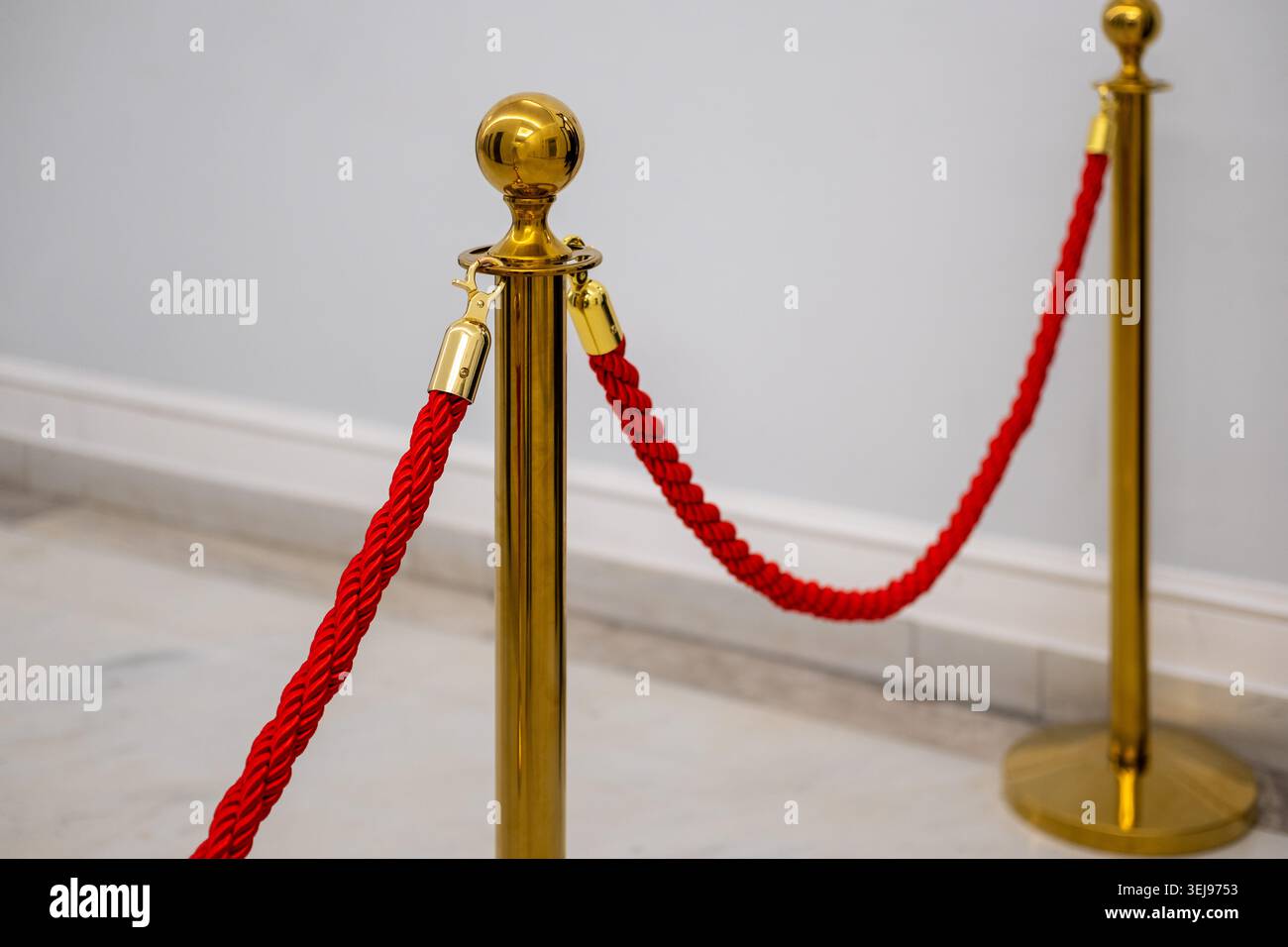 Il montante in metallo dorato con una corda di velluto ritorto rosso si erge su un pavimento in marmo in un ambiente interno. Foto Stock