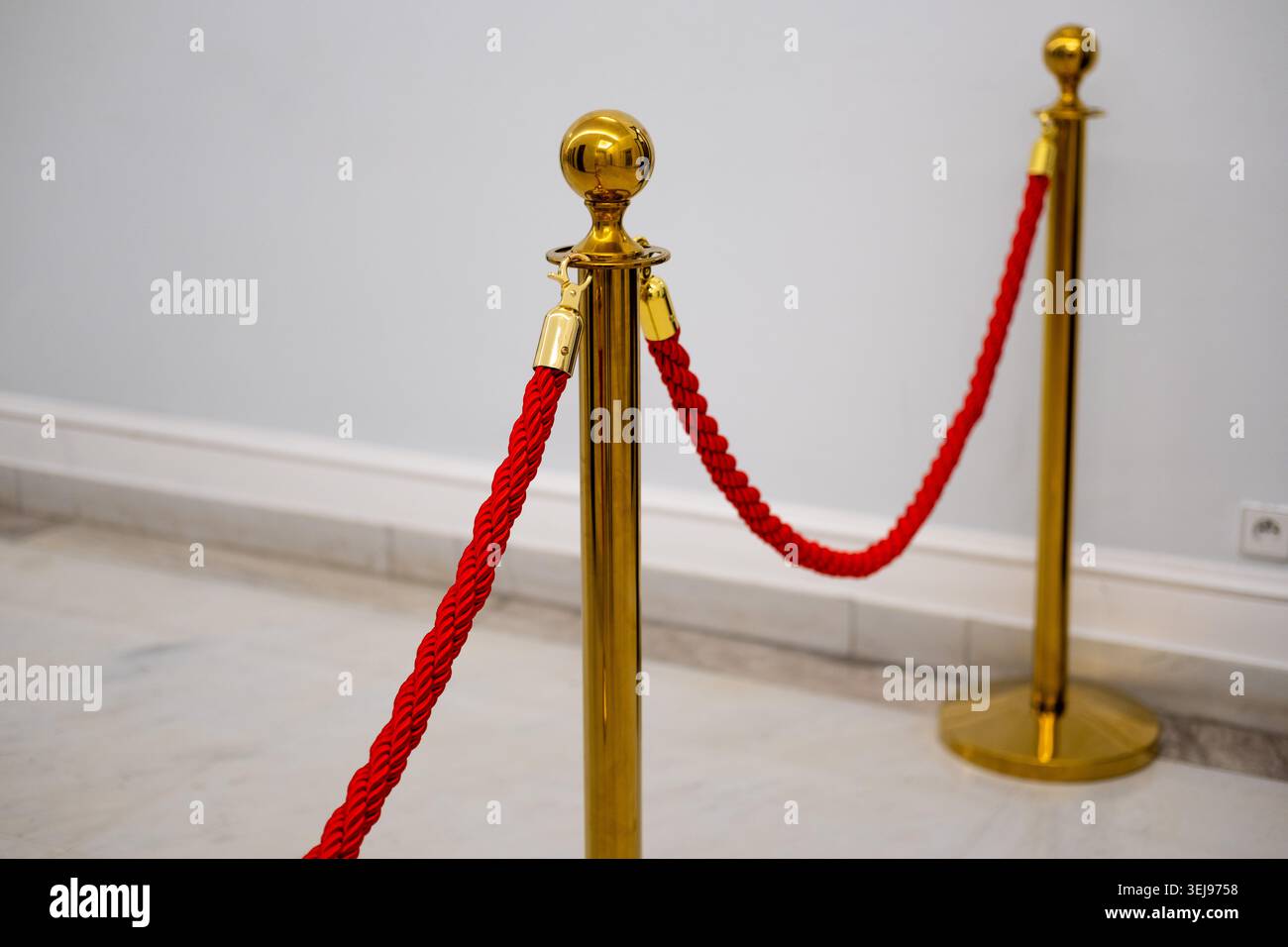 Palo in metallo dorato con una corda intrecciata rossa è collocato su un pavimento di marmo chiaro in un locale. Foto Stock