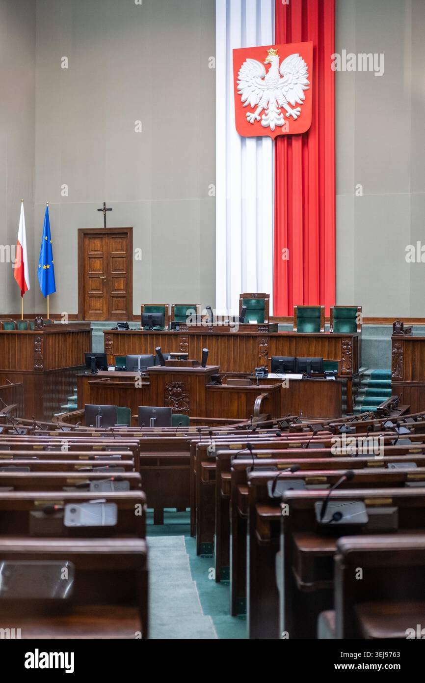Le scrivanie e le sedie vuote in legno si affacciano sul podio principale sotto lo stemma polacco della sala di discussione del Sejm. Foto Stock
