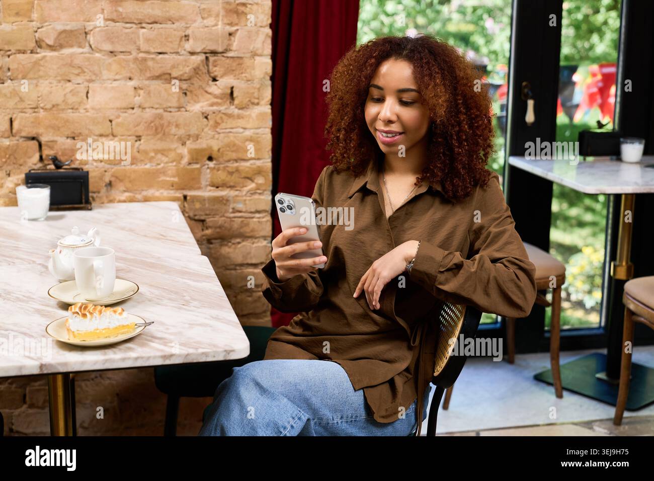 La giovane donna si diverte a trascorrere il tempo in un elegante bar, a controllare i messaggi e ad assaporare il dessert. Foto Stock