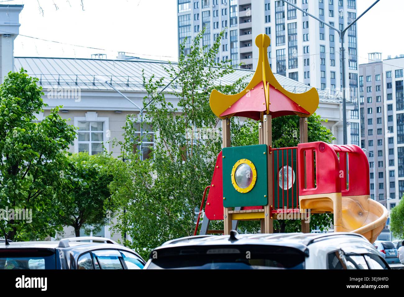 Parco giochi dai colori vivaci circondato da paesaggi urbani e veicoli in un vivace ambiente di quartiere Foto Stock