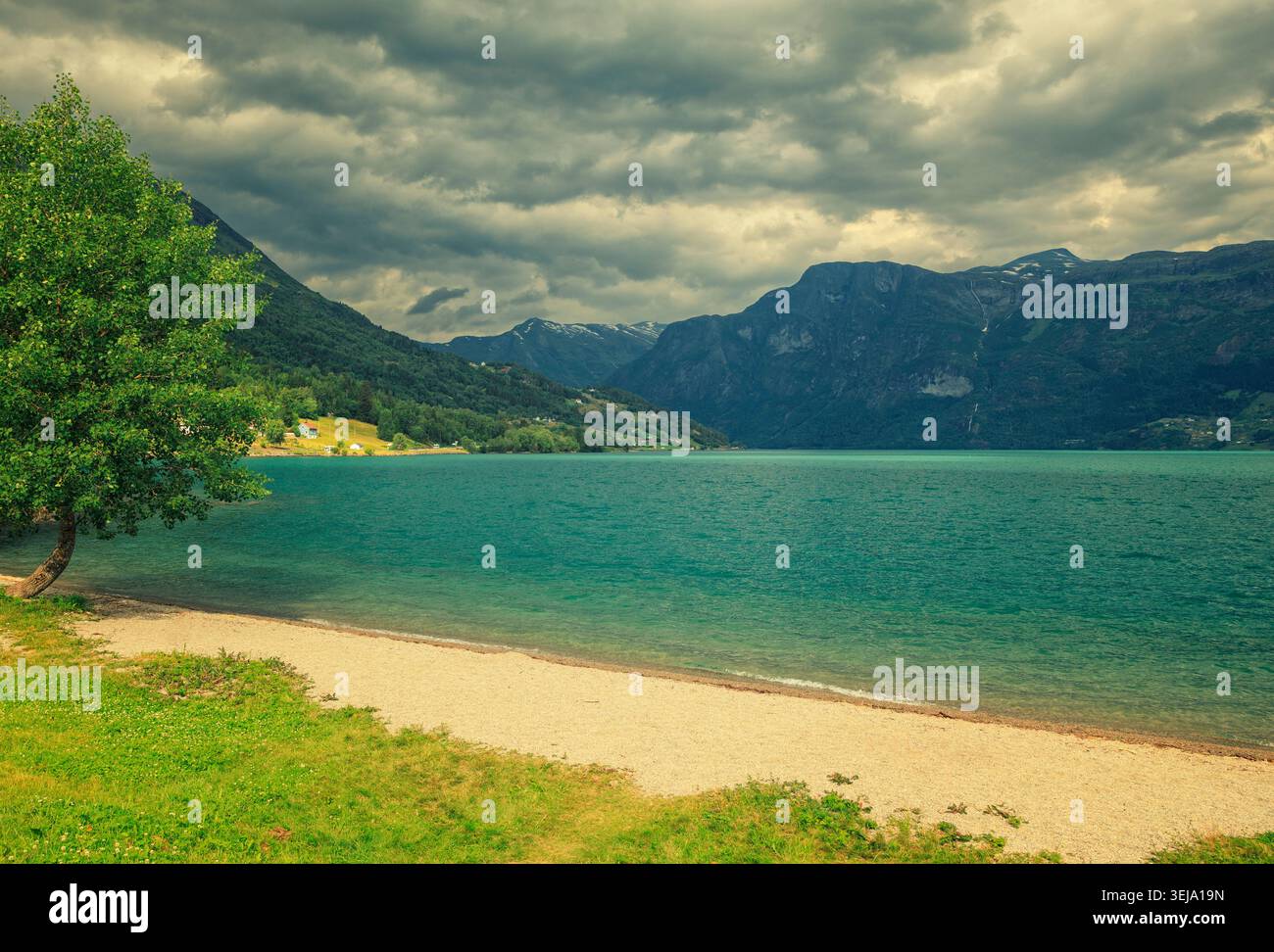 Oppstryn, Norvegia - 28.06.2024: Acque turchesi del lago glaciale con montagne e nuvole di tempesta sotto un cielo spettacolare. Foto Stock