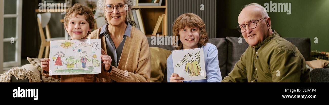 Intestazione della coppia senior con figli che mostra disegni di famiglia Foto Stock