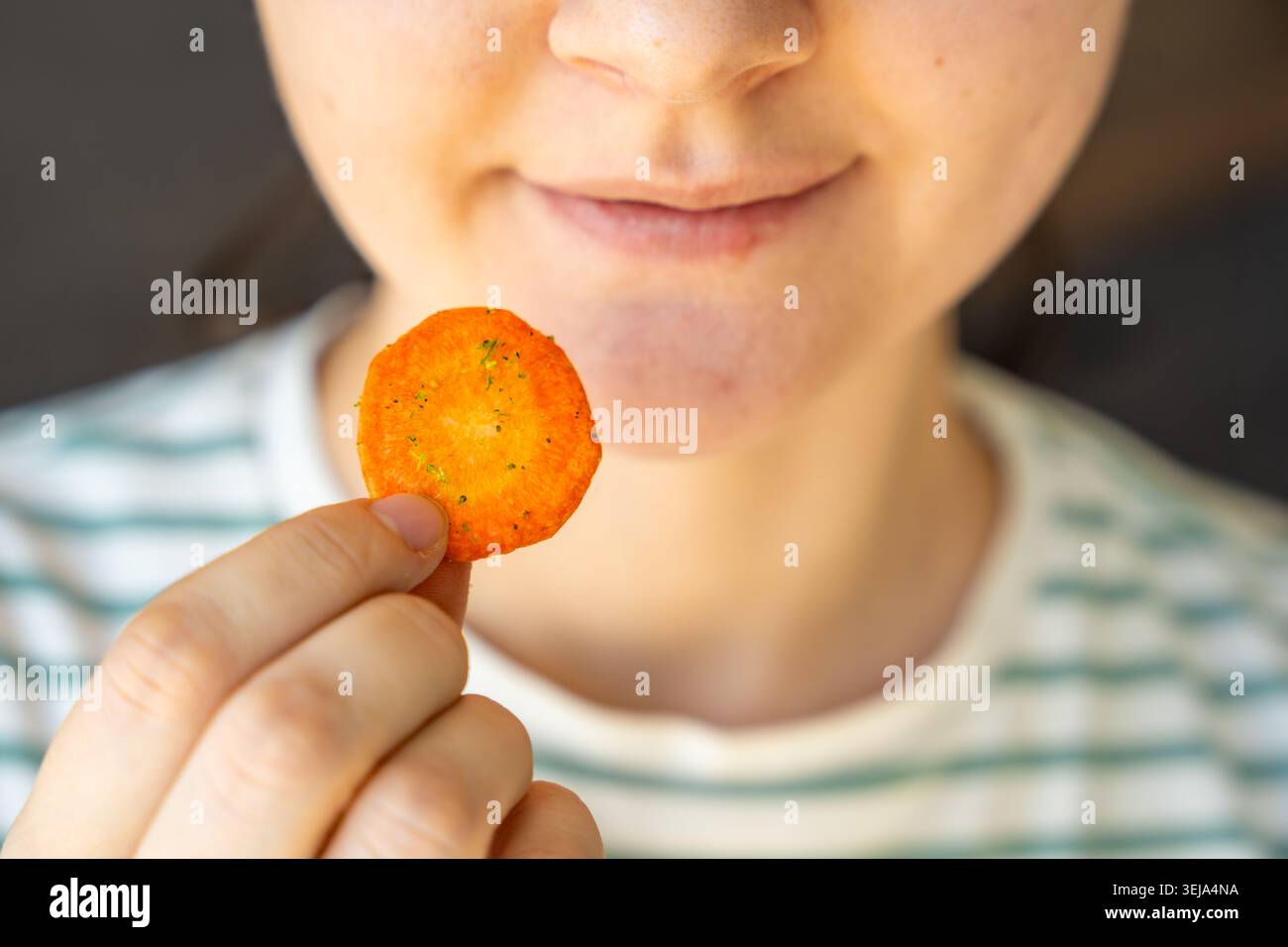 Donna che mangia carota come spuntino sano a casa. Un'alimentazione pulita e una dieta attenta con patatine vegetali naturali. Foto Stock