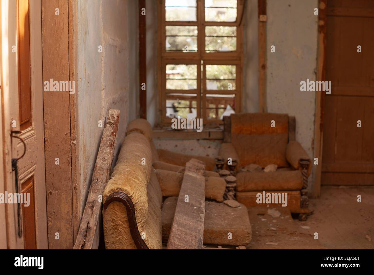 Un divano vintage danneggiato e una poltrona abbinata sono lasciati in una stanza abbandonata con pareti in intonaco sgretolato e pavimento coperto di detriti. Foto Stock