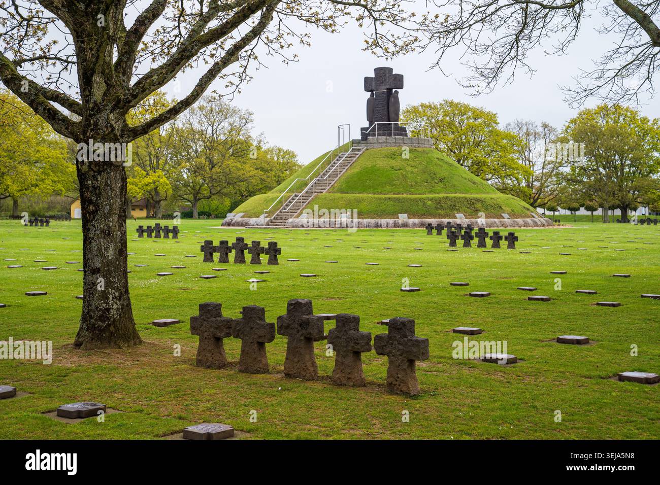 Un gruppo di pietre scure attraversa in primo piano sul prato verde del cimitero militare di la Cambe in Normandia. Sullo sfondo sorge il grande circolo Foto Stock