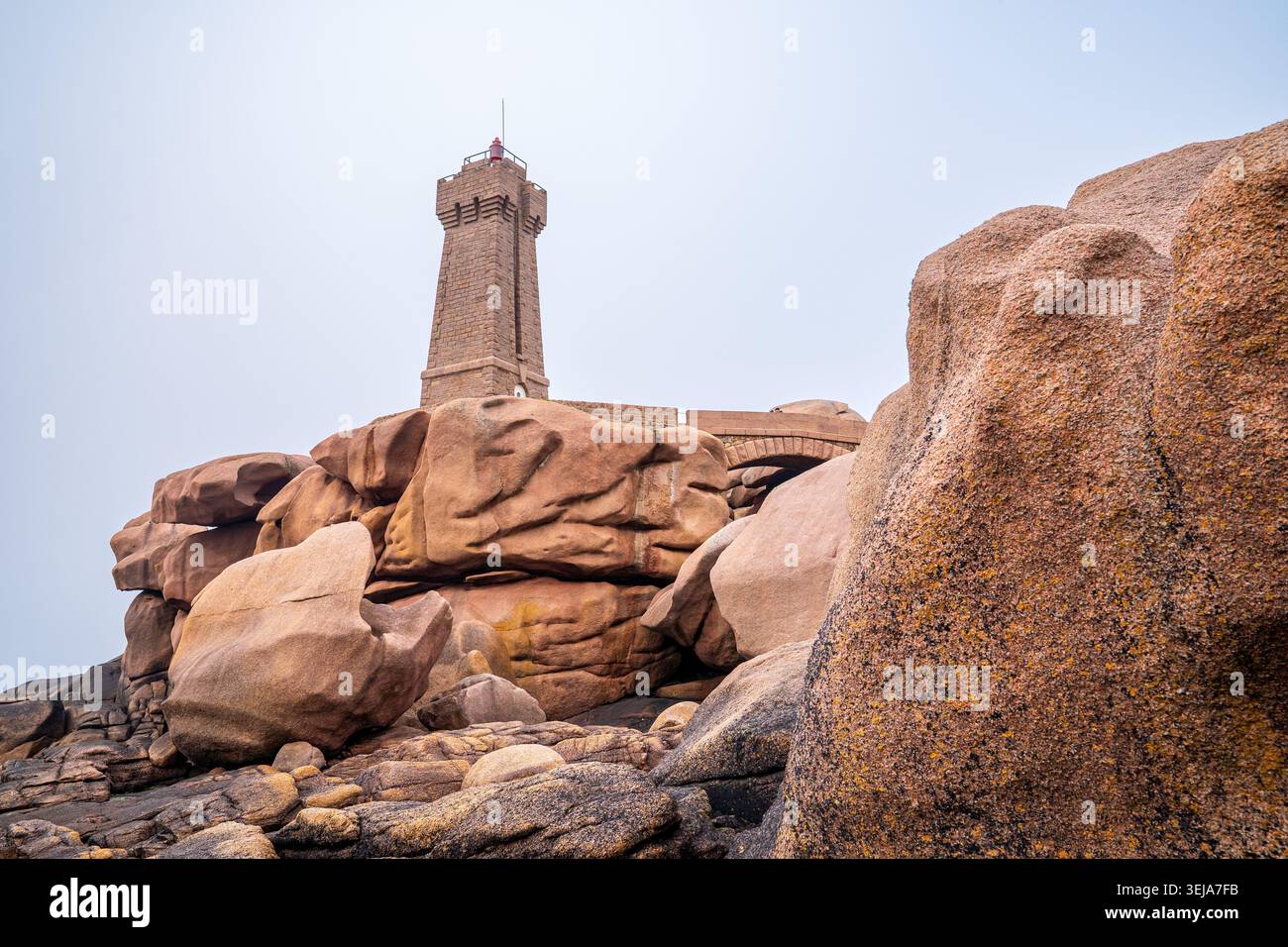 Una prospettiva ad angolo basso mette in evidenza le imponenti scogliere e i grandi massi di granito rosa a Ploumanac'h. Il faro di pietra di Mean Ruz sta sulla somma Foto Stock