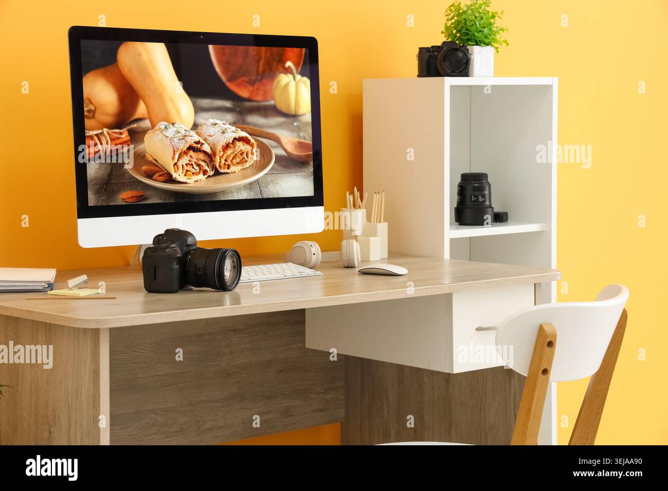 Postazione di lavoro del fotografo con computer, fotocamera e cuffie vicino alla parete gialla in studio Foto Stock