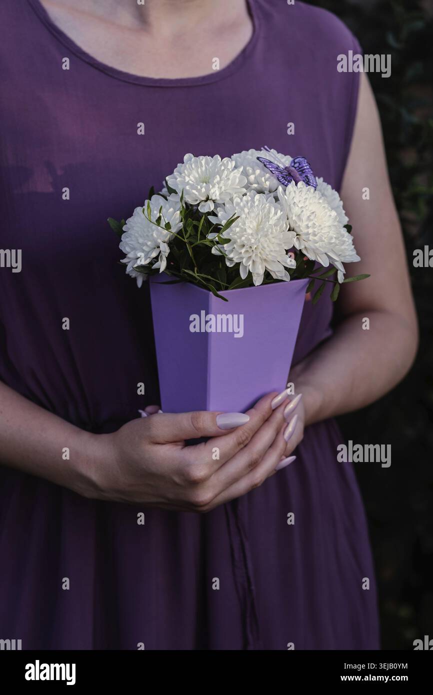 Elegante bouquet di crisantemo bianco in scatola regalo viola con vegetazione lussureggiante e farfalla ornamentale. Decorazioni floreali moderne per saluti, feste o feste Foto Stock