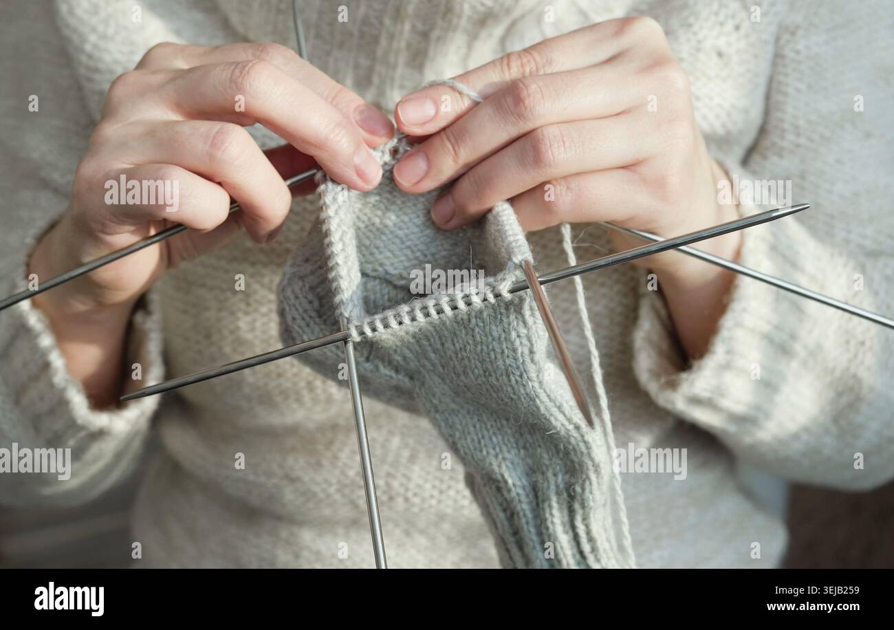 Una donna accogliente in maglia calda si diverte a lavorare a maglia a casa in inverno. Primo piano Foto Stock