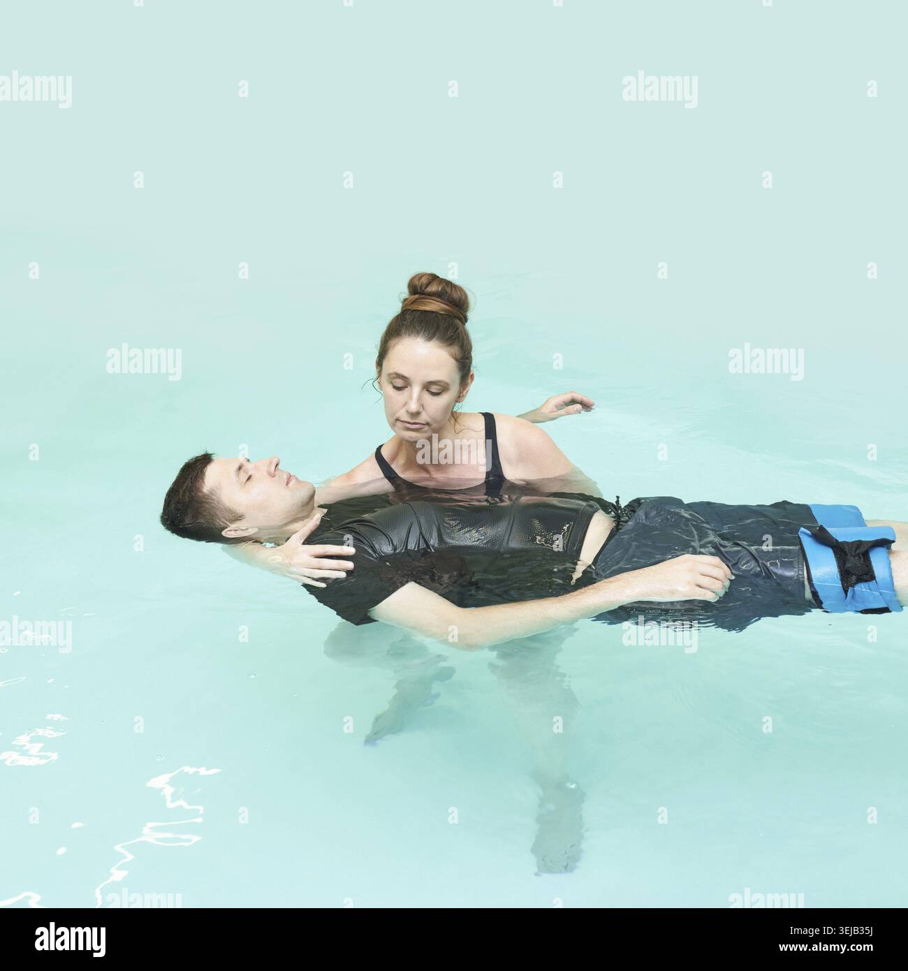 Terapista femminile che conduce terapia acquatica con giovane maschio caucasico in piscina Foto Stock