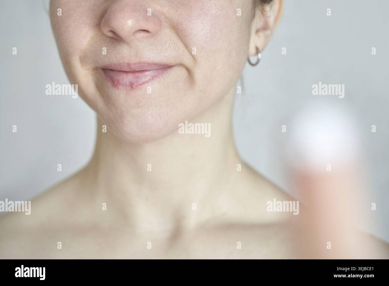Giovane donna caucasica con un sorriso sottile che applica crema per la pelle, mettendo in risalto la bellezza naturale e la sicurezza Foto Stock