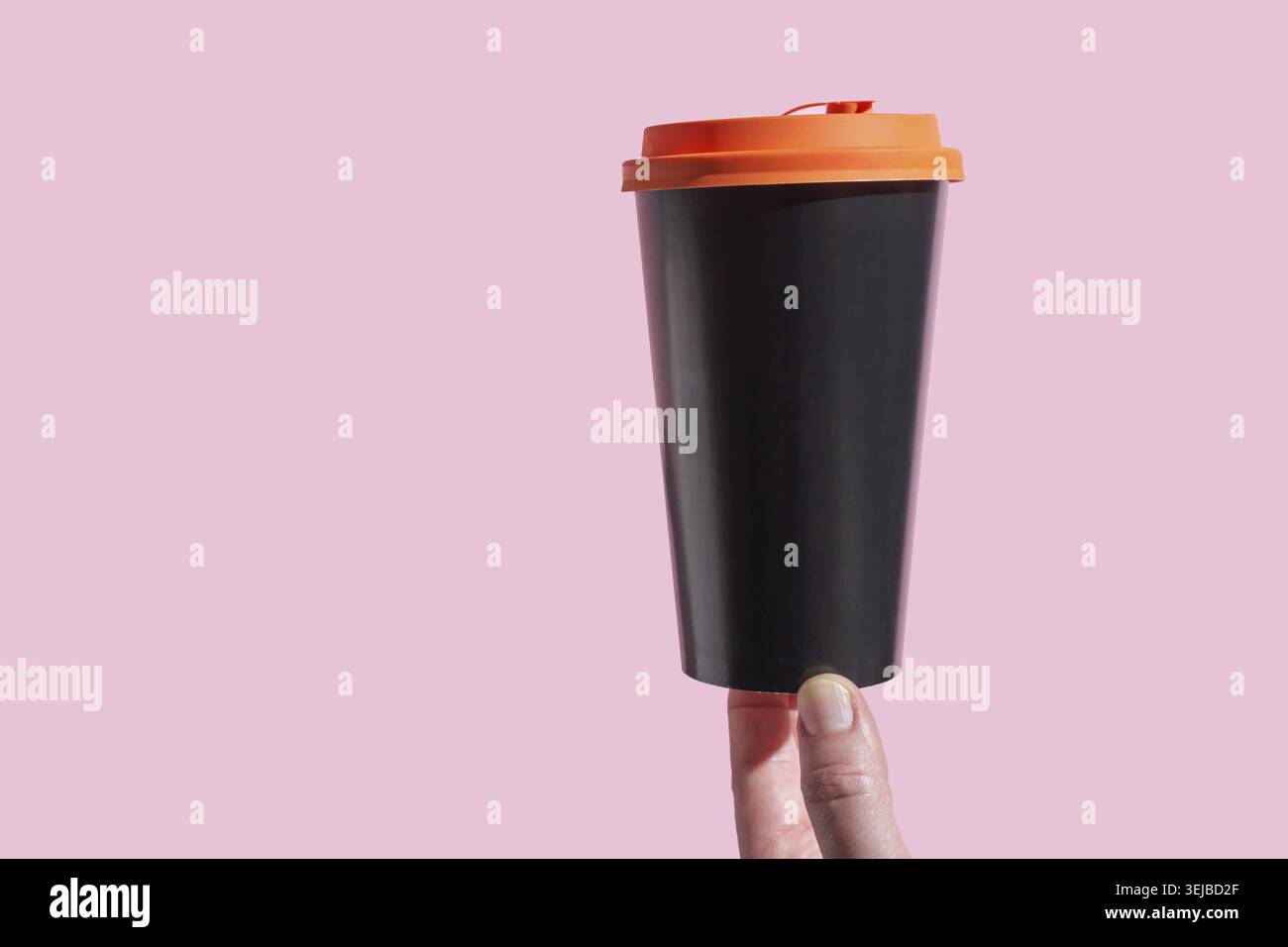 Tazza da caffè nera riutilizzabile con coperchio arancione tenuto a mano su sfondo rosa Foto Stock