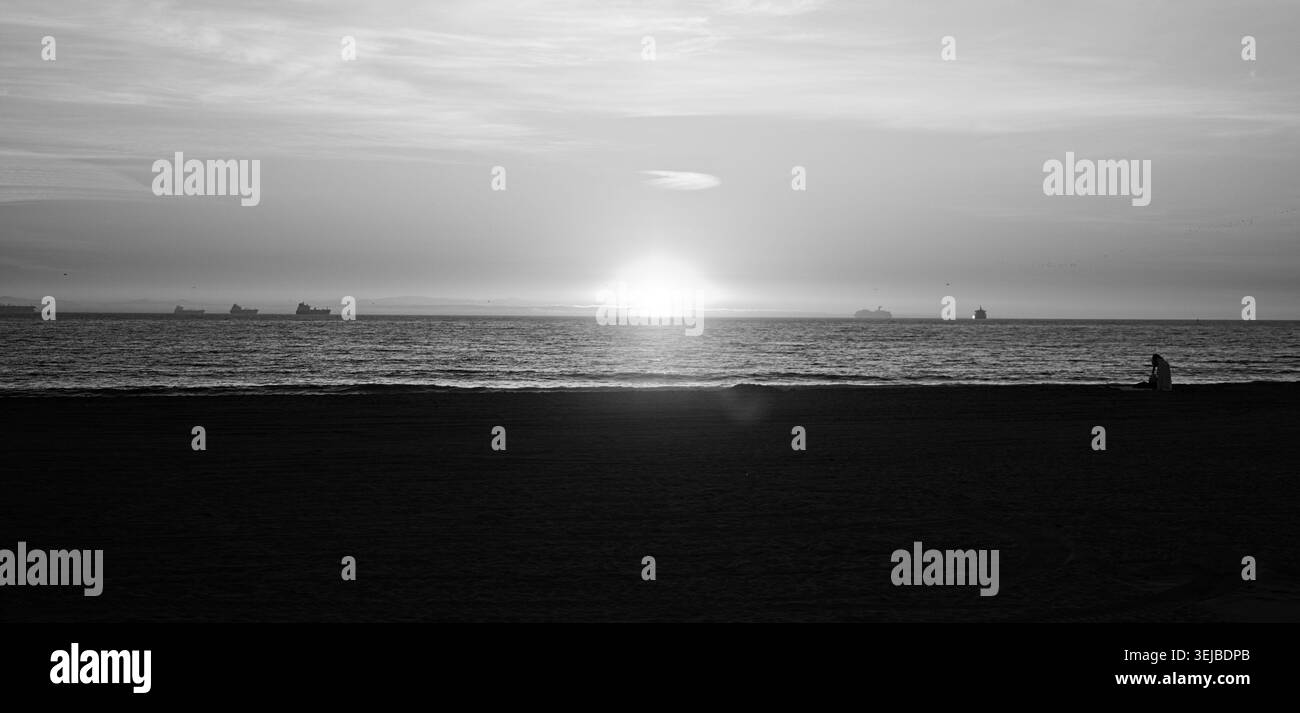 Tramonto dorato sull'Oceano Pacifico a Sunset Beach, California, con onde calme, cielo scintillante e riflessi caldi che creano una tranquilla scena costiera. Foto Stock