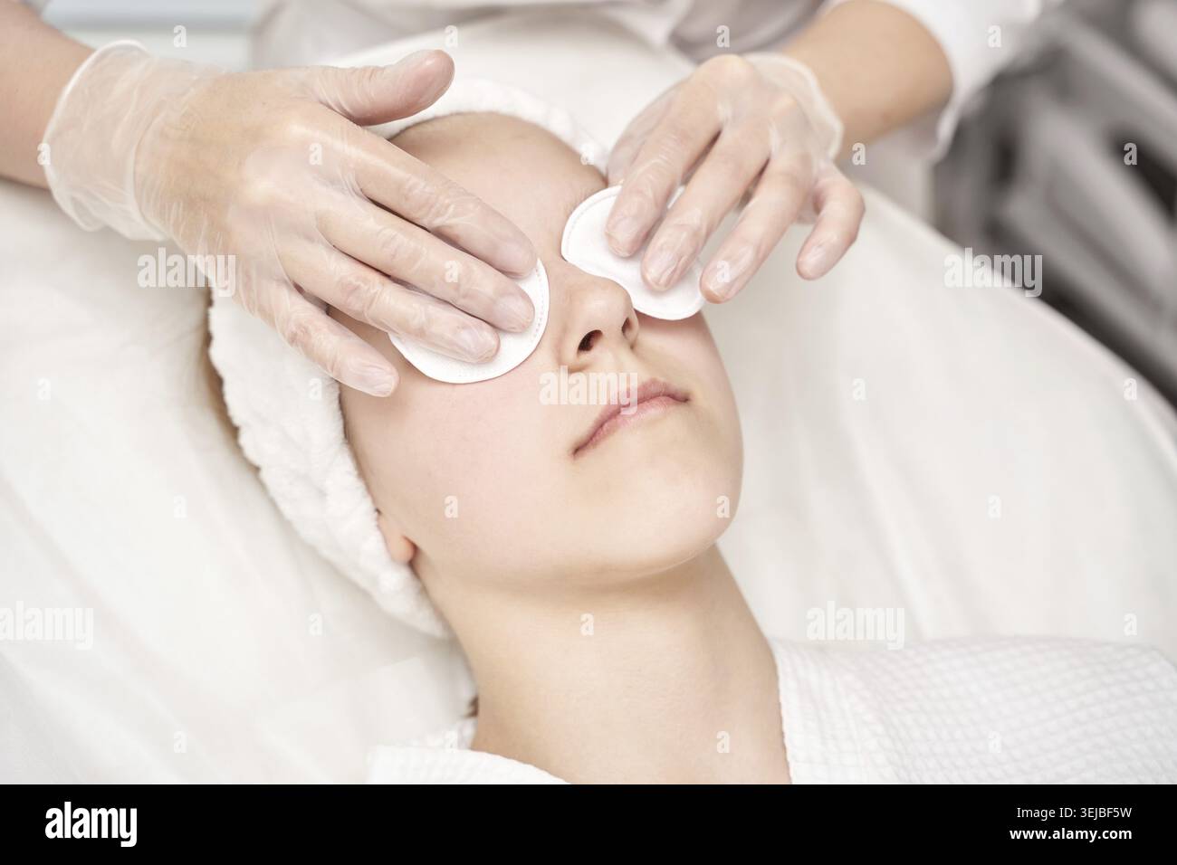 Giovane donna caucasica che riceve un trattamento viso spa con tamponi per gli occhi e mani con guanti in un ambiente rilassante Foto Stock