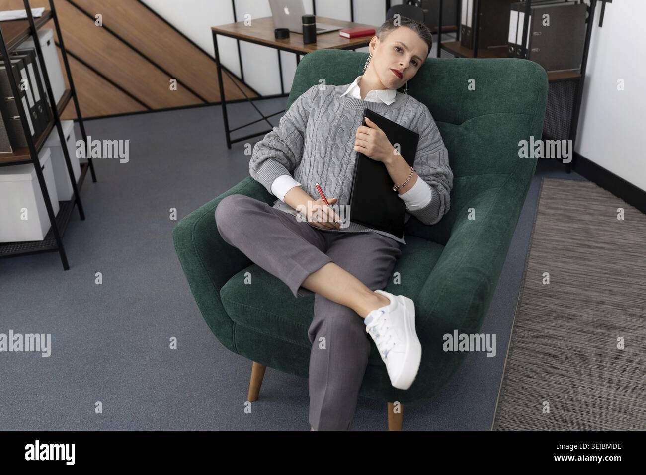 Una donna d'affari con un taglio corto sta riposando sul lavoro in una poltrona Foto Stock