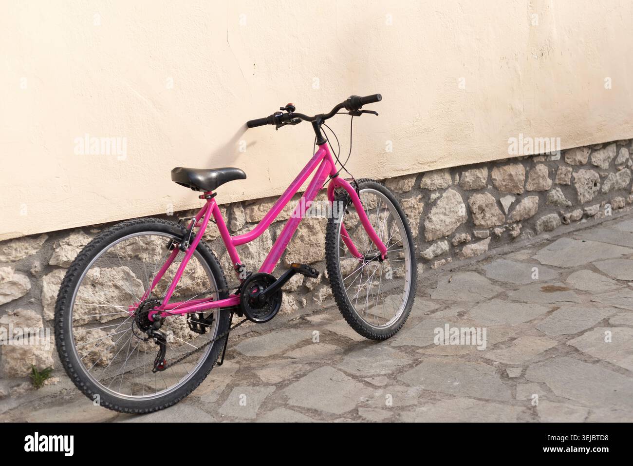 Foto dettagliata a livello degli occhi di un passaggio rosa brillante attraverso una mountain bike appoggiata su una parete in stucco beige con base in pietra su una strada asfaltata in IMG  Foto Stock