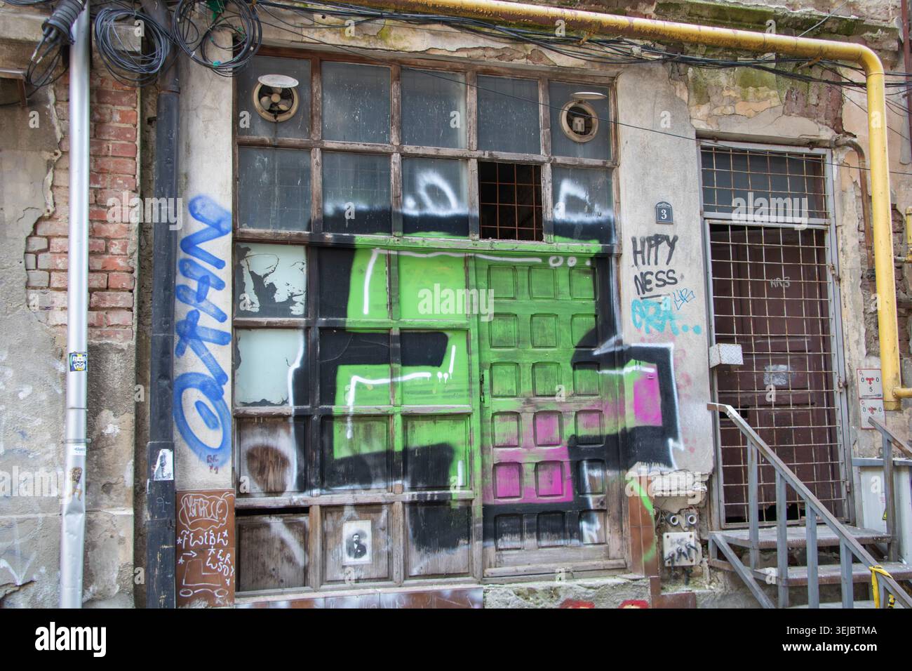Facciata di un vecchio edificio urbano deteriorato con finestre rotte, graffiti e porte industriali intemprate a Bucuresti, Romania - 15 marzo 2026 Foto Stock