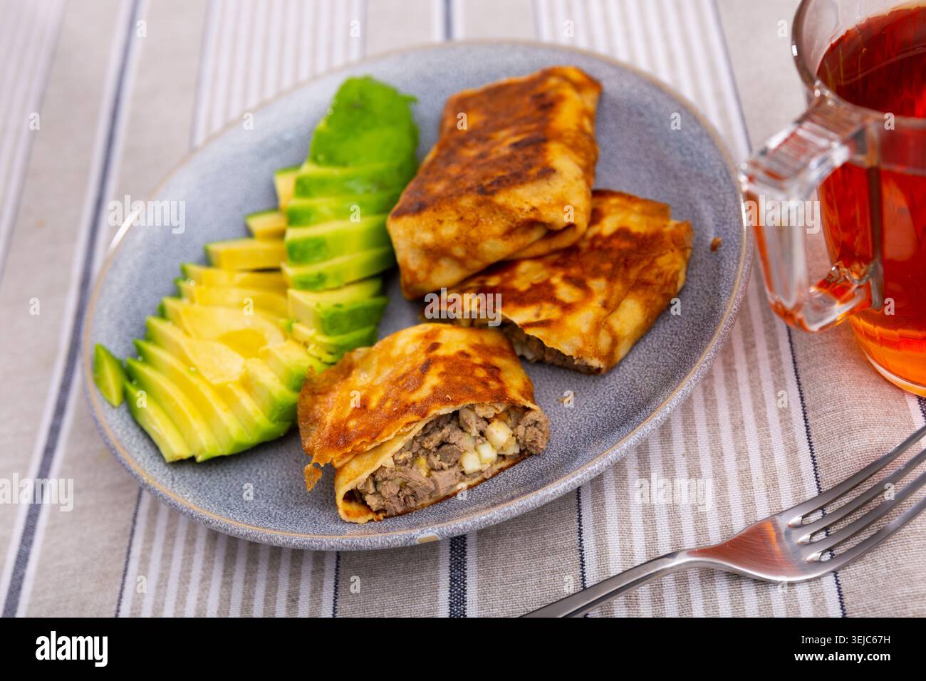 Ci sono pancake con ripieno di fegato e uova sul piatto, integrati con avocado tritato a metà Foto Stock