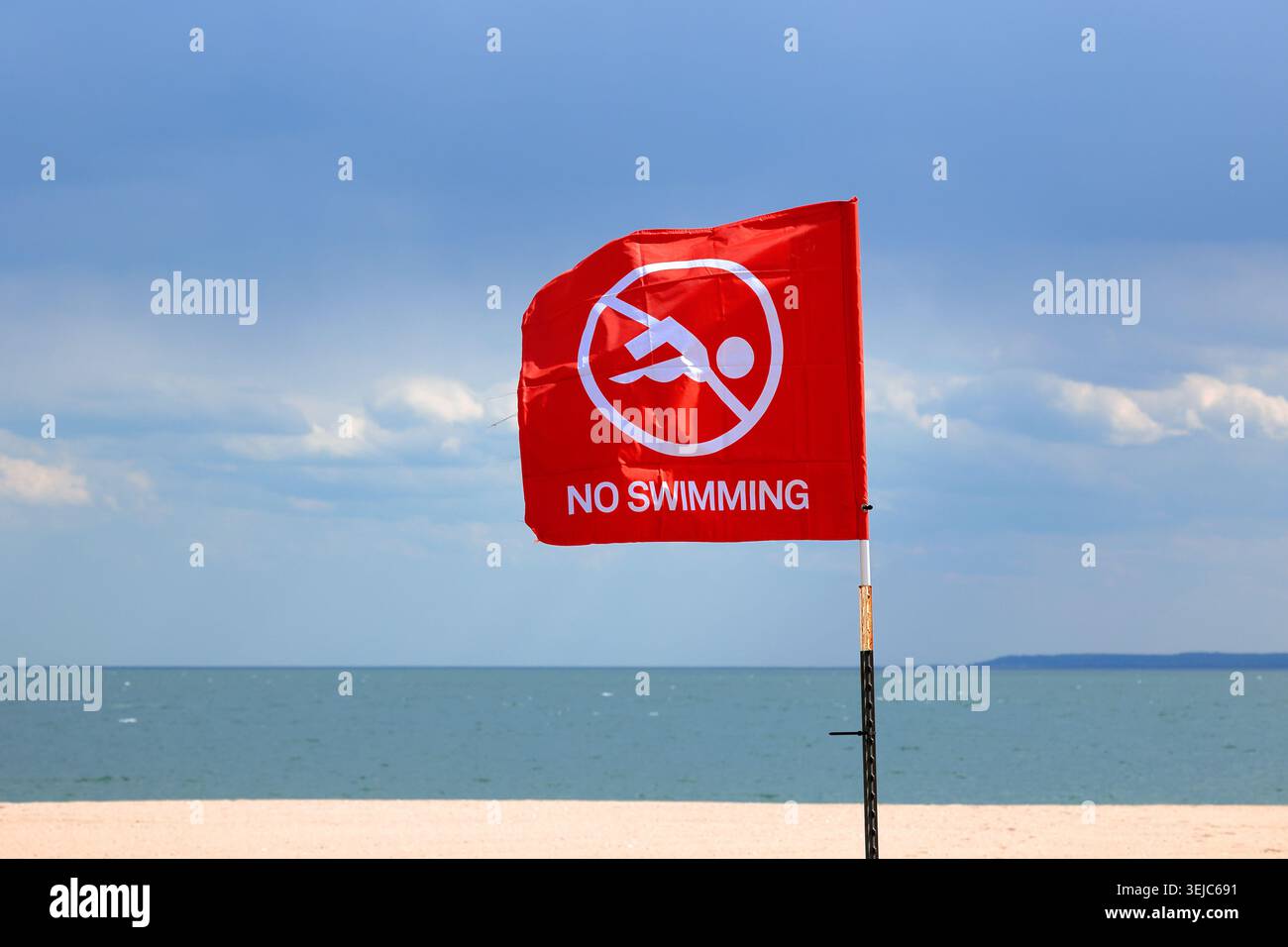 Una bandiera rossa non nuotare su una spiaggia. La bandiera di avvertimento sulla spiaggia avverte i naviganti che l'acqua è chiusa, fuori dai limiti per nuotare a causa di pericoli, tra cui quelli alti Foto Stock