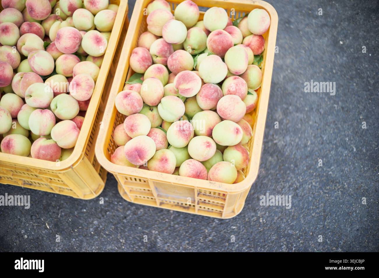 Le foto mostrano pesche all'inizio dell'estate in casse gialle e patate novelle in ciotole rosse in un mercato locale, catturando l'autentico fascino del prodo crudo di stagione Foto Stock